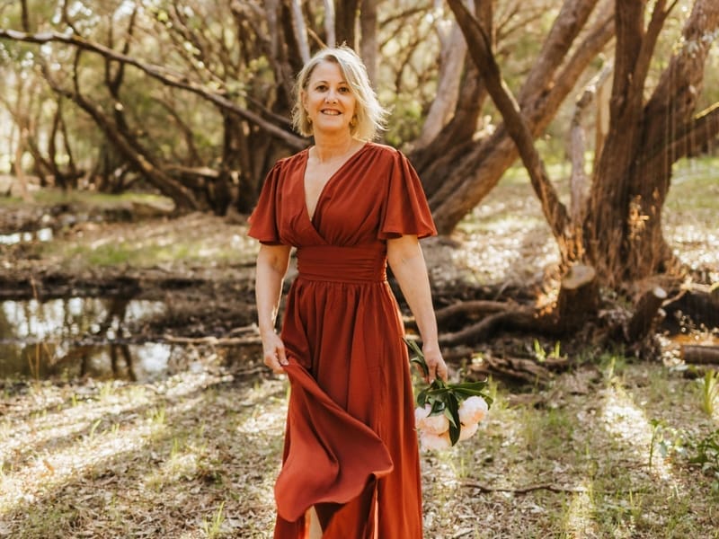 Beth Louise Marriage Celebrant wearing an dark ochre frock standing in front of a tree smiling