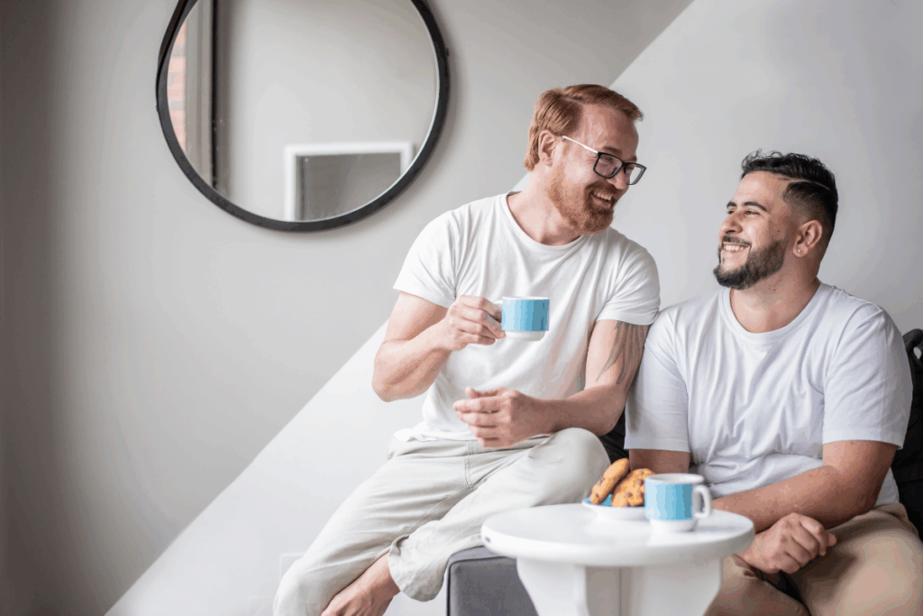 Two men a gay couple looking happy and relaxed as they share a cup of tea and biscuits